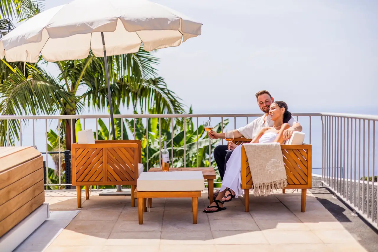 Couple relaxing on the terrace lounge sofa under palm trees, Villa Crossdeira Madeira